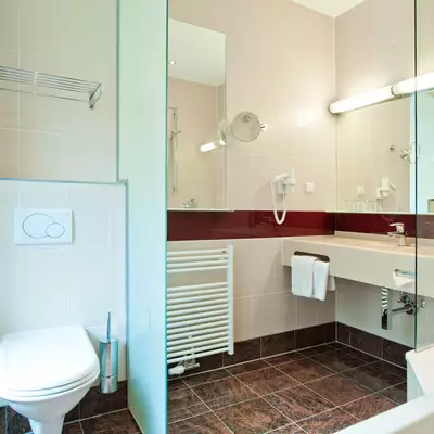Ein modernes Badezimmer mit Dusche, Waschbecken und WC. Wandspiegel und Haken für Handtücher sind vorhanden. Eine Badewanne ist ebenfalls sichtbar. Die Wände sind in neutralen Farben gehalten, und der Boden ist dunkel gefliest.