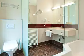 Ein modernes Badezimmer mit Dusche, Waschbecken und WC. Wandspiegel und Haken für Handtücher sind vorhanden. Eine Badewanne ist ebenfalls sichtbar. Die Wände sind in neutralen Farben gehalten, und der Boden ist dunkel gefliest.