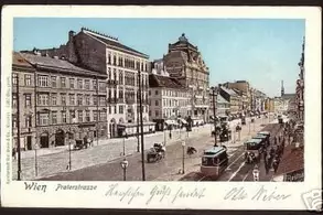 Straßenansicht der Proleterstraße in Wien, mit historischen Gebäuden, Straßenbahnen und Fahrzeugen. Die Szene vermittelt einen Eindruck des urbanen Lebens und der Architektur der Zeit. Es herrscht lebhaftes Treiben auf der Straße.