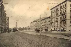 Eine historische Aufnahme einer Wiener Straße mit dem Namen Praterstraße. Auf der Straße sind Pferdekutschen und Menschen zu sehen, während elektrische Oberleitungen über den Weg verlaufen. Die Architektur der Gebäude zeugt von vergangener Pracht.