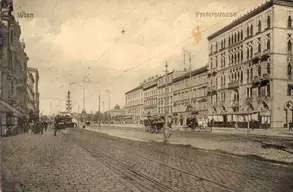 Eine historische Aufnahme einer Wiener Straße mit dem Namen Praterstraße. Auf der Straße sind Pferdekutschen und Menschen zu sehen, während elektrische Oberleitungen über den Weg verlaufen. Die Architektur der Gebäude zeugt von vergangener Pracht.