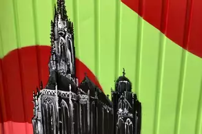 Eine Wand mit buntem Hintergrund in Grün und Rot, auf dem eine detaillierte Schwarz-Weiß-Darstellung einer Kirche mit mehreren Türmen und Spitzen zu sehen ist. Die Architektur wirkt historisch und filigran, umgeben von kräftigen Farben.