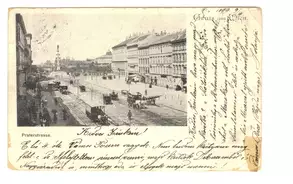 Historische Postkarte von der Praterstraße in Wien, circa 1899. Die Ansicht zeigt eine breite Straße mit Pferdefuhrwerken sowie Gebäuden beiderseits. In der Mitte steht ein Denkmal, im Hintergrund sind weitere Gebäude sichtbar. Handgeschriebene Notizen sind am rechten Rand sichtbar.