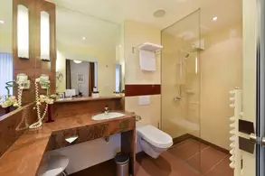 Ein modernes Badezimmer mit einem Waschtisch aus Marmor, Spiegel und einer Dusche aus Glas. Es gibt einen Toilettenbereich, Handtücher hängen an der Wand, und neben dem Waschbecken stehen Pflegeprodukte in einem dekorativen Arrangement. Sanfte Beleuchtung schafft eine angenehme Atmosphäre.