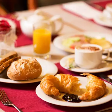Ein liebevoll gedeckter Frühstückstisch mit einer Tasse Kaffee, frischen Croissants und einem Glas Orangensaft.